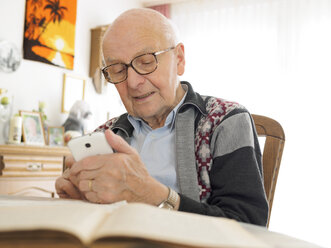 Alter Mann sitzt am Tisch und benutzt ein Mobiltelefon - LAF001314