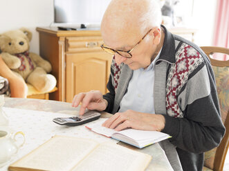 Alter Mann sitzt am Tisch und sucht in einem Notizbuch nach einer Telefonnummer - LAF001316