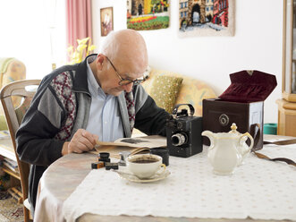 Alter Mann sitzt am Tisch und beschäftigt sich mit einer alten Kamera - LAF001323