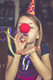 Kleines Mädchen mit Clownsnase und Mütze bläst Luftschlangen - SARF001323