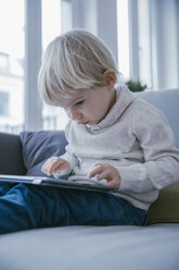 Little boy sitting on the couch playing with digital tablet - MFF001463