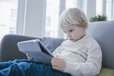 Kleiner Junge sitzt auf der Couch und schaut sich etwas auf einem digitalen Tablet an - MFF001464