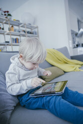 Kleiner Junge sitzt auf der Couch und spielt mit einem digitalen Tablet - MFF001467