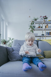 Kleiner Junge sitzt auf der Couch und spielt mit einem digitalen Tablet - MFF001468