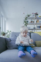 Little boy sitting on the couch playing with digital tablet - MFF001468