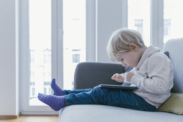 Kleiner Junge sitzt auf der Couch und spielt mit einem digitalen Tablet - MFF001469