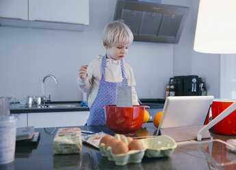 Little boy standing in the kitchen baking with help of digital tablet - MFF001472