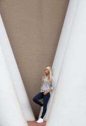 Porträt eines blonden weiblichen Teenagers, der sich an eine Betonsäule lehnt - WWF003830