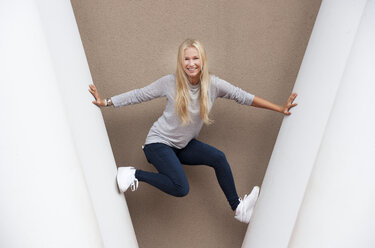 Portrait of smiling blond female teenager between concrete columns - WWF003738