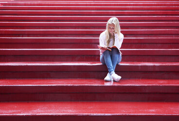 Weiblicher Teenager sitzt auf einer roten Treppe und liest - WWF003756