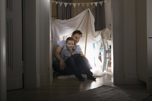 Vater und Sohn sitzen abends in einem selbstgebauten Zelt zu Hause und benutzen ein digitales Tablet - PDF000685