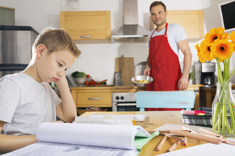 Junge sitzt am Küchentisch mit seinen Hausaufgaben, lizenzfreies Stockfoto