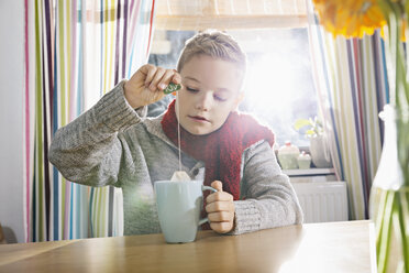 Boy having a cold sitting in the kitchen with cup of tea - PDF000760