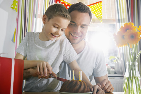 Vater und Sohn schneiden Geburtstagstorte an, lizenzfreies Stockfoto