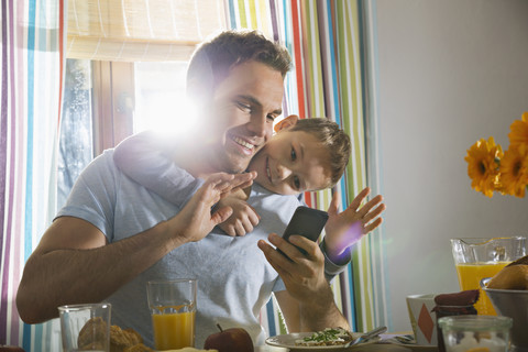 Vater und Sohn sitzen am Frühstückstisch und machen ein Selfie, lizenzfreies Stockfoto