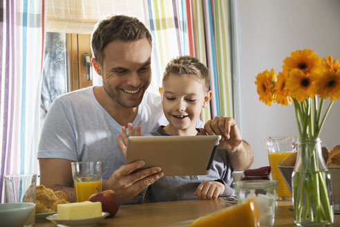 Father and son sitting at breakfast table using digital tablet - PDF000763