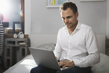 Man sitting on bed at home using laptop - PDF000703