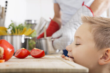 Lächelnder Junge mit Blick auf Tomatenscheiben auf Küchenbrett - PDF000741