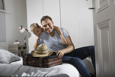 Father and son sitting on bed with suitcase and straw hat - PDF000737