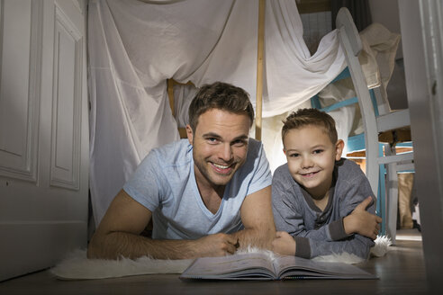 Vater und Sohn mit Buch auf dem Boden liegend im selbstgebauten Zelt zu Hause - PDF000723