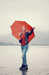 Austria, Mondsee, teenage girl with red umbrella standing at lakeshore - WWF003779