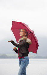 Austria, Mondsee, teenage girl with red umbrella standing at lakeshore - WWF003780