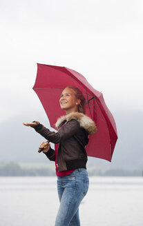 Österreich, Mondsee, junges Mädchen mit rotem Regenschirm am Seeufer stehend - WWF003780