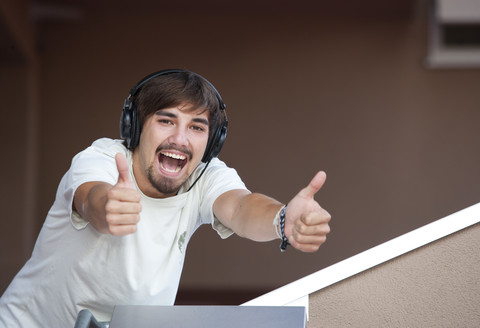 Porträt eines jungen Mannes mit Kopfhörern und Daumen nach oben, lizenzfreies Stockfoto