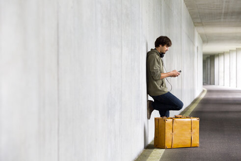 Mann mit Lederkoffer und Smartphone wartet in einem Parkhaus - WWF003712