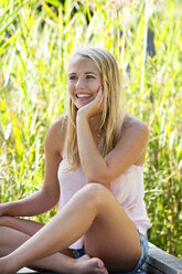 Portrait of smiling young woman sitting on wooden boardwalk - WWF003845