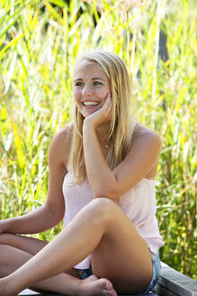 Porträt einer lächelnden jungen Frau, die auf einer Holzpromenade sitzt - WWF003845