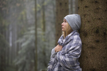 One female teenager with blanket and hat leaning on tree trank - WWF003793