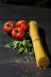 Spaghetti, Basilikum und Tomaten auf dunklem Holz - MAEF009690
