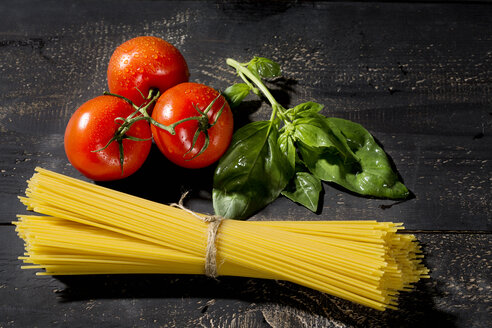 Spaghetti, Basilikum und Tomaten auf dunklem Holz - MAEF009691