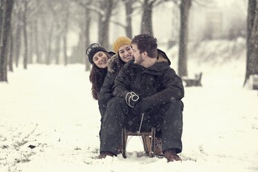 Three friends sitting on sledge in winter - PAF001249