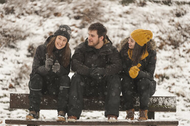 Drei Freunde sitzen in einer Reihe auf einer Holzbank im Winter - PAF001251