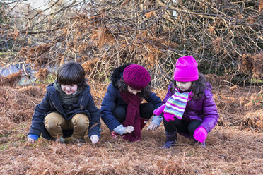 Three children crouching side by side in a park on a winter day - MGOF000052