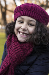 Porträt eines lächelnden kleinen Mädchens mit Zahnlücke, das Wollmütze und Schal trägt - MGOF000056