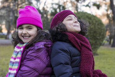 Porträt von zwei glücklichen kleinen Mädchen, die an einem Wintertag Rücken an Rücken in einem Park stehen - MGOF000060