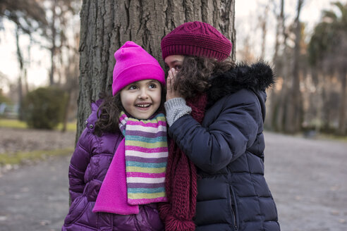 Mädchen erzählt einem anderen Mädchen ein Geheimnis in einem Park an einem Wintertag - MGOF000063