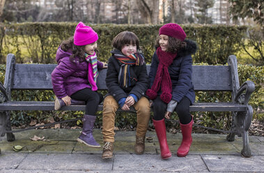 Drei Kinder sitzen an einem Wintertag auf einer Bank in einem Park - MGOF000067
