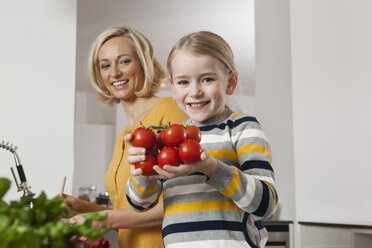 Mother with daughter holding tomatoes in kitchen - RBF002387