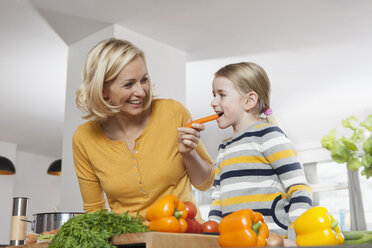 Mother with daughter eating carrot in kitchen - RBF002388