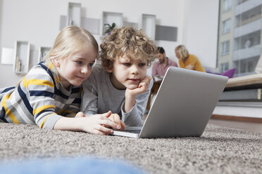 Bruder und Schwester liegen auf dem Boden und benutzen einen Laptop - RBF002406