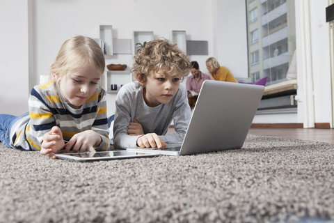 Bruder und Schwester liegen auf dem Boden und benutzen Laptop und digitales Tablet, lizenzfreies Stockfoto