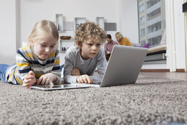 Brother and sister lying on floor using laptop and digital tablet - RBF002407