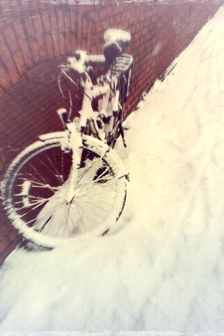 Schneebedecktes Fahrrad lehnt an der Wand, lizenzfreies Stockfoto