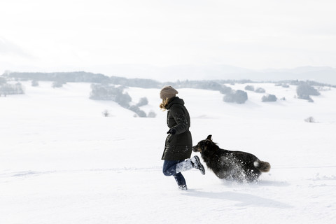 Germany, Baden-Wuerttemberg, Waldshut-Tiengen, woman and dog running in snow stock photo