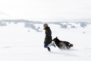 Germany, Baden-Wuerttemberg, Waldshut-Tiengen, woman and dog running in snow - MIDF000055