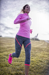 Spanien, Gijon, sportliche junge Frau läuft auf einer Wiese - MGOF000082